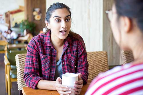 two women sit together at a coffee shop and talk
