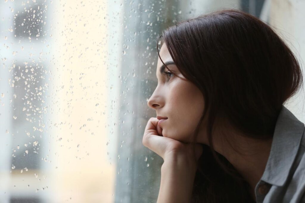 a woman sits and stares through a window while wondering about heroin side effects
